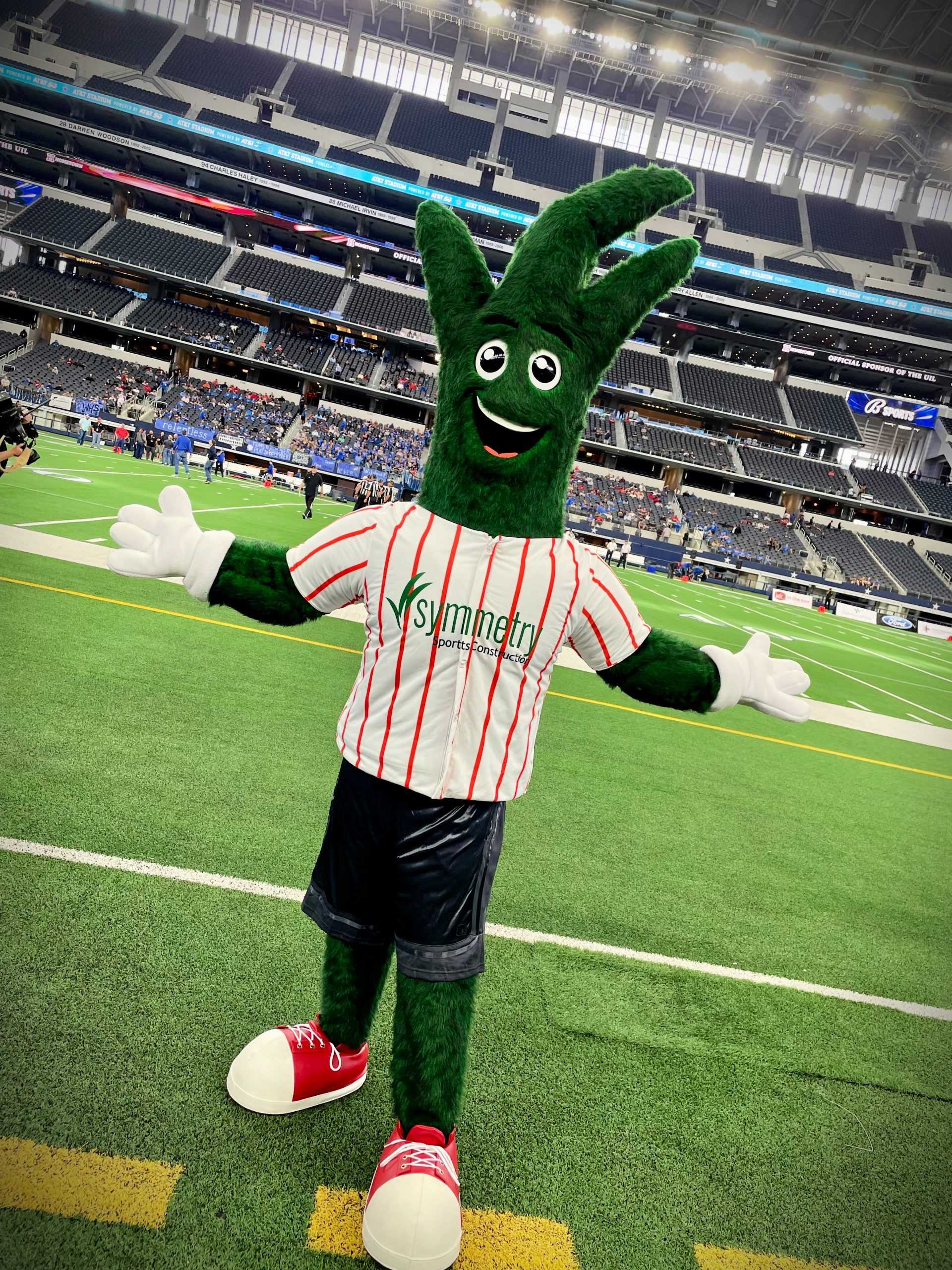 Symmetry Sports Construction Company mascot standing on a field that Symmetry performed artificial turf maintenance on