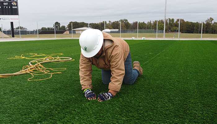 A Symmetry Sports Construction technician doing maintenance on a synthetic sports field